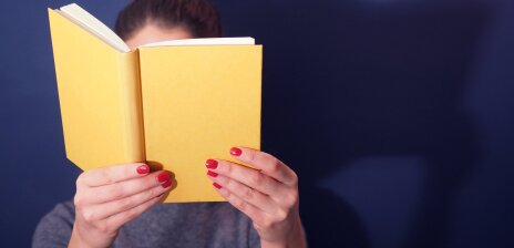 A woman holds a book in front of her face.