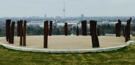Der Blick von oben auf die Aussichtsplattform Metalhenge: Mehrere Metall-Stelen stehen in einem Kreis auf einer runden Platte. Im Hintergrund ist der Panoramablick auf Bremen zu erkennen.