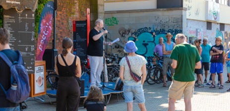 Eine Person trägt etwas vor auf einer mobilen, kleinen Bühne unter freiem Himmel an der Weserpromenade. 
