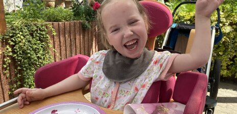 Ein lachendes Mädchen am Esstisch im Garten. 