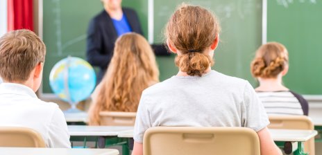 Ein Lehrer steht an einer Tafel vor einer Schulklasse.