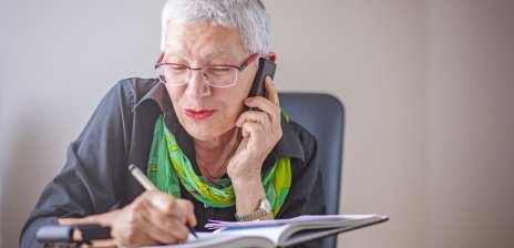 Eine Seniorin schreibt etwas in eine Notizbuch, während sie telefoniert.