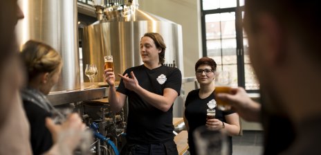 Ein Mitarbeiter und eine Mitarbeiterin der Union Brauerei führen eine Brauereiführung für Gäste durch.