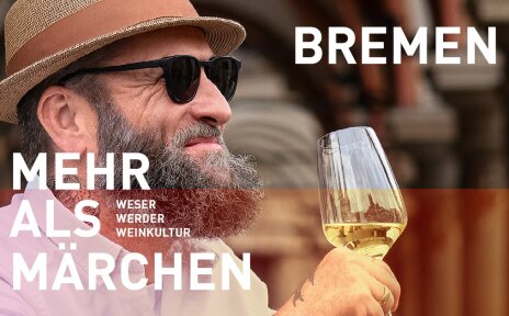 Ein lächelnder Mann vor einem historischen Gebäude. Er hat einen Vollbart, trägt einen Strohhut und eine Sonnenbrille und hält ein Glas mit Weißwein in der Hand. Schriftzug im Bild: "Bremen - Mehr als Märchen. Weser, Werder, Weinkultur". 