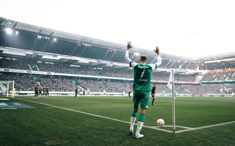 Ein Fußballspieler steht in einem grünen Trikot an der Ecke und schießt einen Ball. 