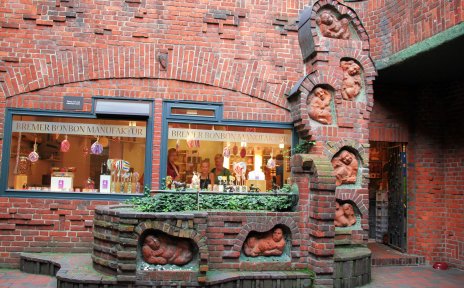 Roter Backsteinbrunnen mit sieben steinernen, in die Wand eingelassenen Figuren drumherum.