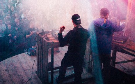 2 DJs stehen auf einer Bühne vor Publikum und legen auf. 