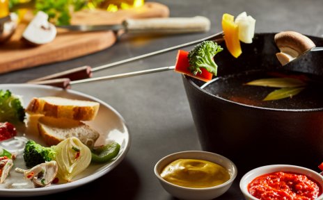 Ein Fonduetöpf mit Tellern voller verschiedener Gemüsearten und Saucen