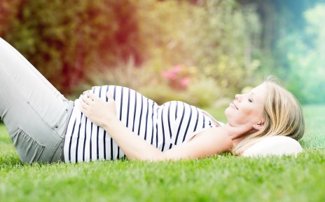 Eine schwangere Frau liegt lächelnd auf einer Wiese (Quelle: fotolia / drubig-photo)