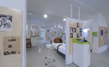 Eine Innenaufnahme aus dem hellen Krankenhausmuseum. Zu sehen sind einige Ausstellungsstücke sowie schwarz-weiß Bilder und Infotexte.