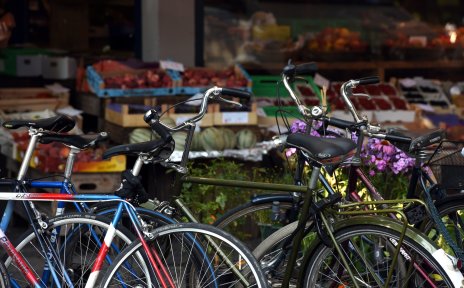 Parkende Fahrräder, im Hintergrund ein Obst- und Gemüsegeschäft mit Warenkörben vor dem Fenster.