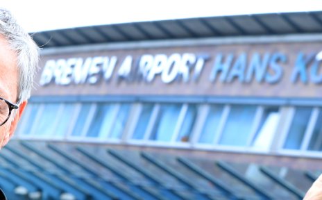 Ein Mann mit runder Brille und Krawatte zeigt auf den neuen Namen am Flughafenterminal