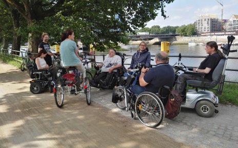 Eine Gruppe von Menschen in Rollstühlen, mit Handbike und Dreirad an der Weser.