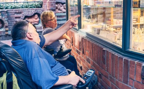 Ein Mann und eine Frau im Rollstuhl vor einem Schaufenster.