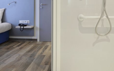 Blick in eine barrierefreie Dusche mit Duschsitz, im Hintergrund ein Hotelzimmer.