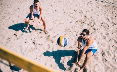 Zwei Männer spielen im Sand Volleyball.