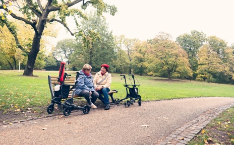 Zwei ältere Damen sitzen auf einer Parkbank und unterhalten sich fröhlich.