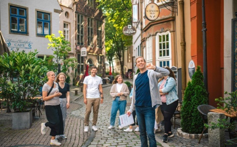 Ein Mann führt eine Gruppe durch das Schnoorviertel vorbei an kleinen Häusern in einer schmalen Gasse.