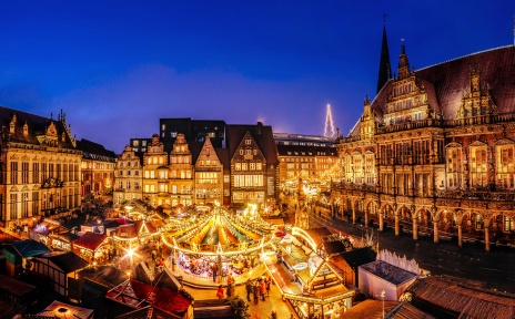 Eine historische Kulisse mit einem Weihnachtsmarkt, der in der Abendstimmung leuchtet.