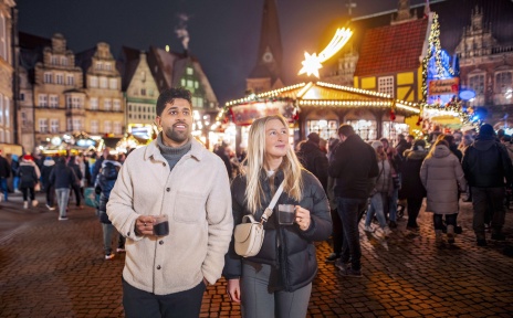 Ein Mann und eine Frau laufen mit Tassen in der Hand über den Bremer Weihnachtsmarkt.