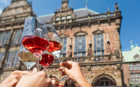 Vier Personen stoßen mit einem Weinglas vor dem Bremer Rathaus an.