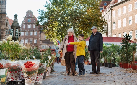 Großeltern gehen mit ihrem Enkel über einen Wochenmarkt.