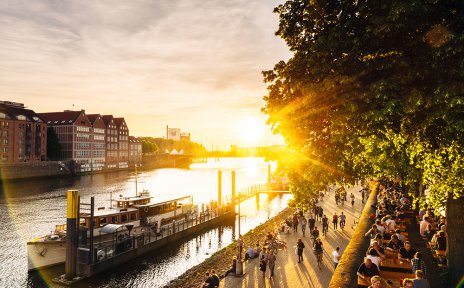Blick auf Schiffe, schlendernde Menschen und Biergärten an der abendlichen Weserpromenade Schlachte 