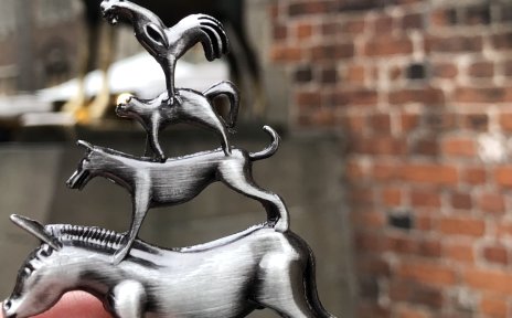Eine Hand, die eine Metallfigur der Bremer Stadtmusikanten vor die echte Bronzefigur der Bremer Stadtmusikanten hält.
