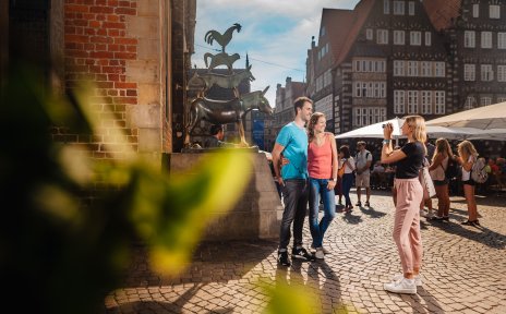 Ein Pärchen steht vor der Bronzestatue der Bremer Stadtmusikanten und lässt sich von einer Frau fotografieren.