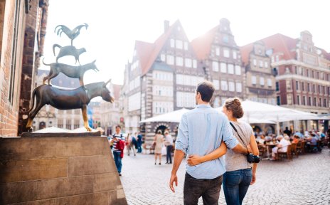 A woman and a man stand in front of the Bremen Town Musicians. 