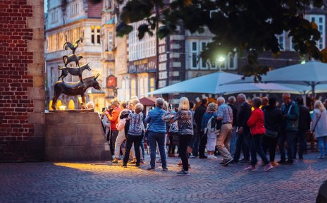 Die Aufnahme zeigt viele Menschen, die am Abend vor der Bronzestatue der Bremer Stadtmusikanten stehen und Bilder machen. 