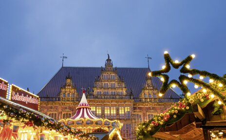 Vor der historischen Kulisse des Bremer Rathauses funkeln weihnachtlich beleuchtete Verkaufsstände und Karussells