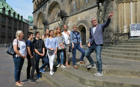 Ein Gästeführer erzählt einer jungen Gruppe bei einer Stadtführung am Dom Wissenswertes über Bremen