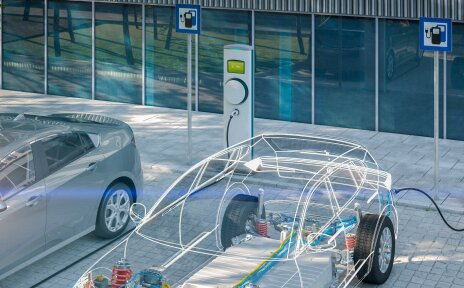 Zwei Elektrofahrzeuge, nur als Rahmen skizziert, stehen auf Parkplätzen mit Ladesäulen. Es wird dargestellt, wie der Strom aus den Ladesäulen in die Fahrzeuge fließt und dort die Akkus auflädt.