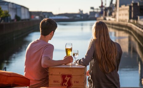 Ein Pärchen sitzt in der Abendsonne auf der Terrasse der Feuerwache in der Überseestadt und blickt auf das Hafenbecken.