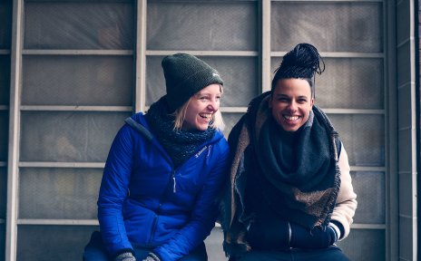 Zwei lachende junge Frauen sitzen nebeneinander.