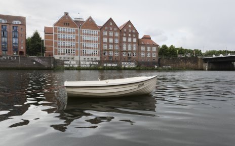 Im Vordergrund ein kleines weißes Boot mit Namen Achim auf der Weser, im Hintergrund die Weserburg