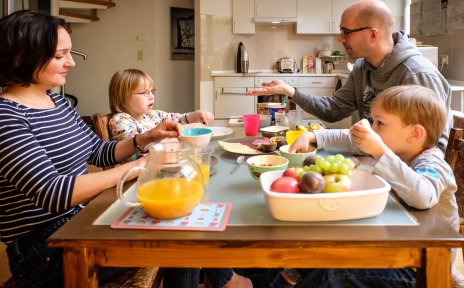 Ein Mann und eine Frau sitzen mit zwei kleinen Kindern am Frühstückstisch. Ein Bild über den Alltag in einer Familie mit behinderten und nicht behinderten Kindern.