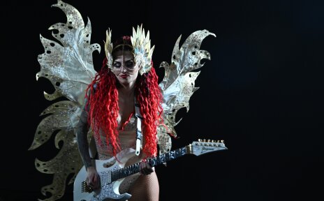 Eine rothaarige Frau trägt ein Kostüm mit Flügeln. Sie spiel E-Gitarre.