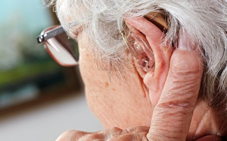 Seitliche Aufnahme einer Seniorin. Sie trägt ein Hörgerät und eine Brille.