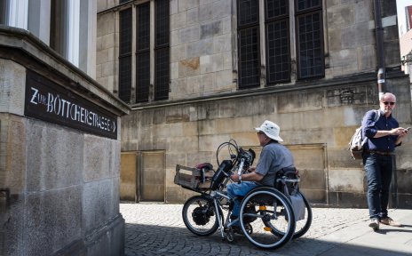 Zwei Männer, einer mit, einer ohne Rollstuhl, links ein Schild mit Aufschrift "Zur Böttcherstraße". (Foto: Nils Protze)