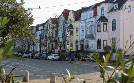 Der Blick fällt auf eine Reihe Altbremer Häuser. Davor parken Autos und es hängen Zweige im Bild.