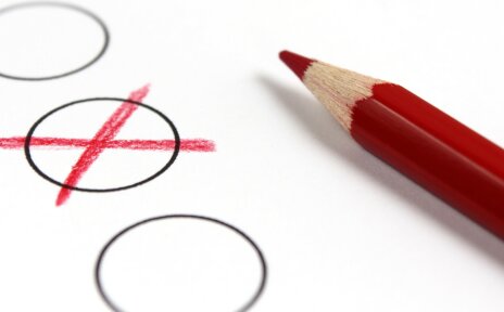 Ein roter Buntstift neben einem mit Kreuz markierten Kreis