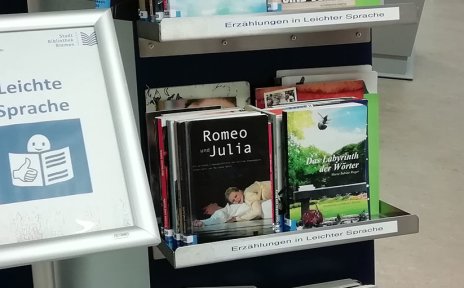 Ein Bücherregal in einer Bibliothek mit Büchern in Leichter Sprache. Davor steht ein Schild mit der Aufschrift "Leichte Sprache".