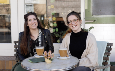 Zwei junge Frauen sitzen vor einem Caféan einem Tisch mit zwei Getränken.