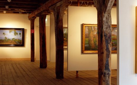 Ein Ausstellungssaal mit Gemälden, Dielenboden und Holzbalken.