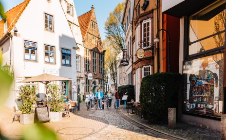 Zwei junge Frauen und zwei junge Männer schieben nebeneinander ihre Räder durch das herbstliche Schnoor-Viertel