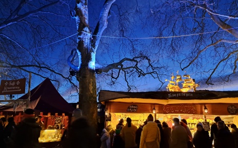 Buden beim historischen Markt auf dem Schlachte-Zauber an der Weserpromenade. Abendstimmung, die Bäume sind blau angestrahlt.