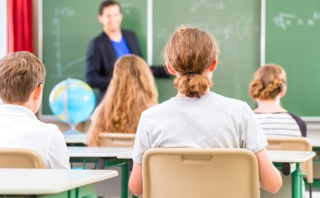 ein Lehrer steht an einer Tafel vor einer Schulklasse 