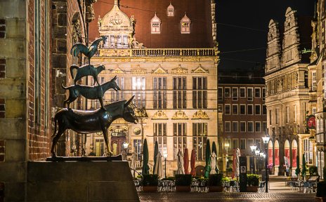 Blick auf die Bremer Stadtmusikanten bei Nacht vor dem Hintergrund des beleuchteten Marktplatzes mit dem Schütting.